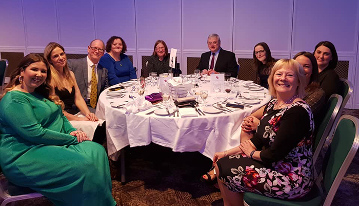 A group of food teachers, chefs and fishmongers sit around a table smiling, at an awards ceremony